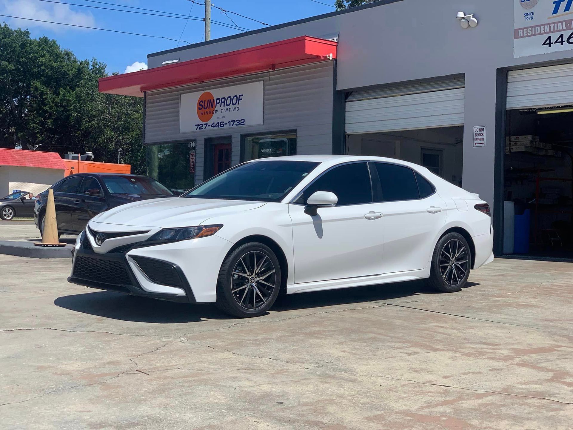 White sedan parked outside sunproof window tinting shop on a sunny day.