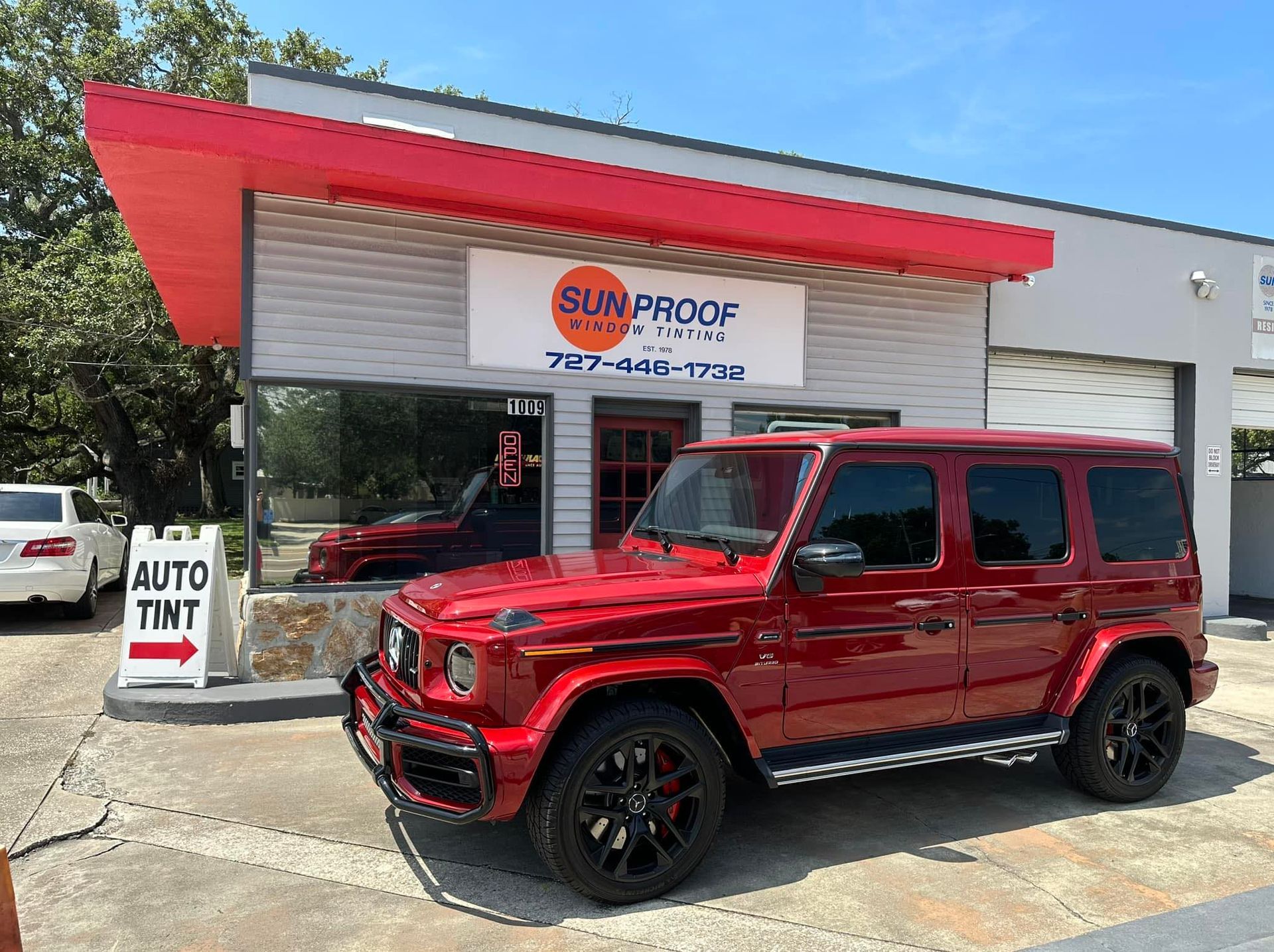 Red SUV parked outside Sun Proof Window tinting storefront with red awning and sign.