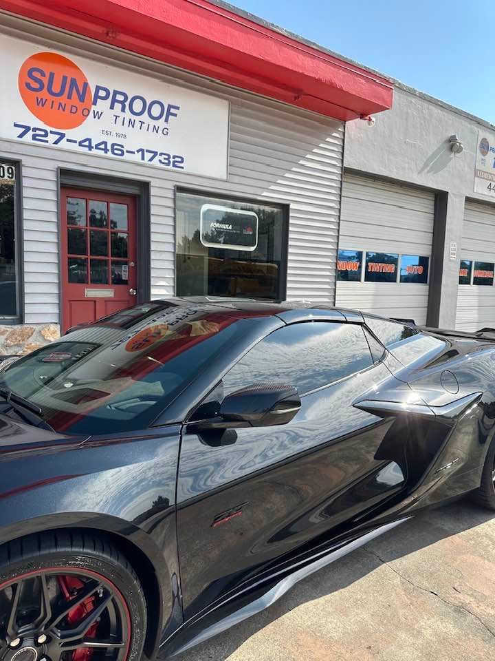 Black sports car parked outside Sun Proof shop with red roof and garage doors