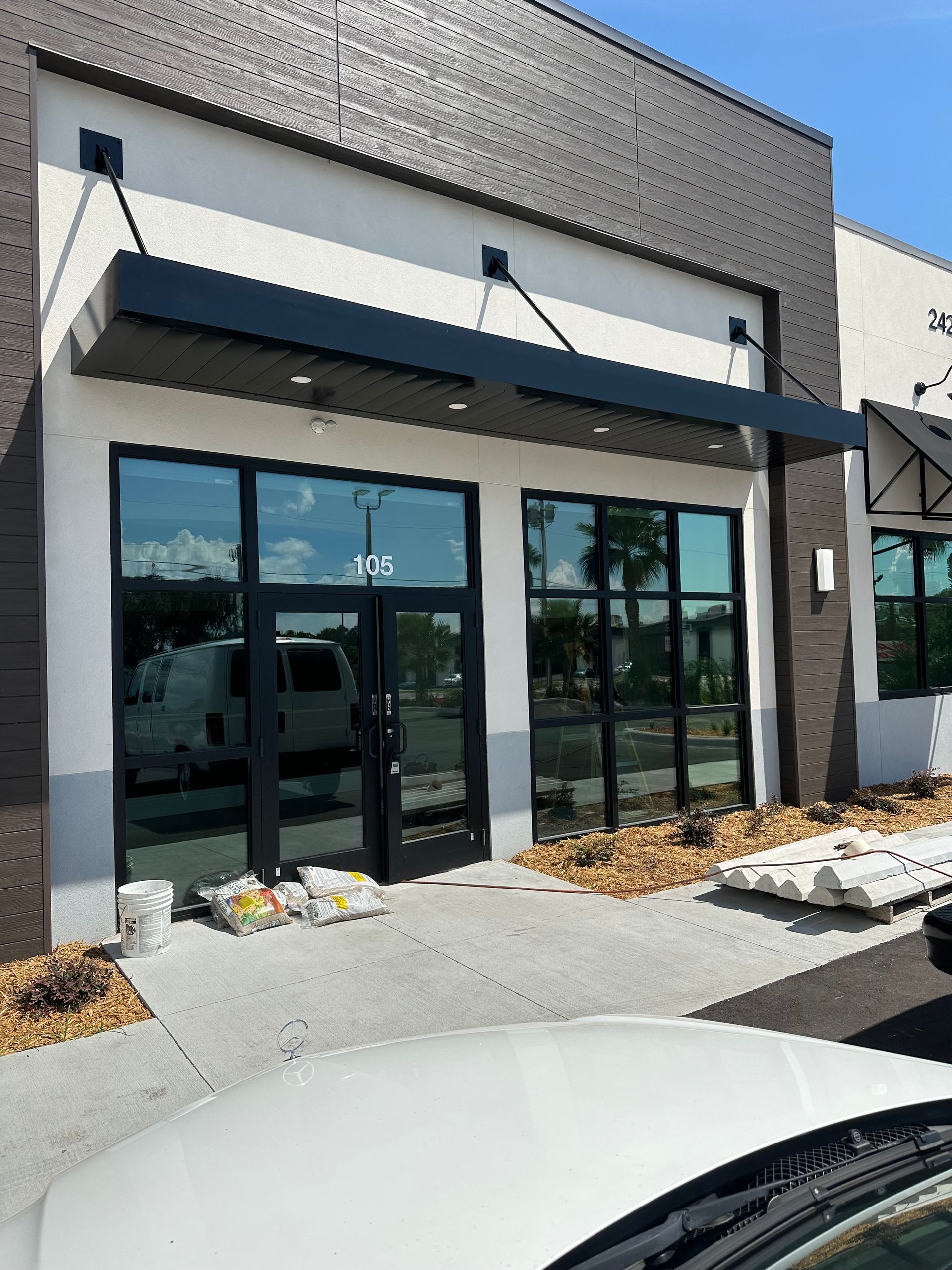 Modern storefront with glass doors, blue awning, and parked cars in front