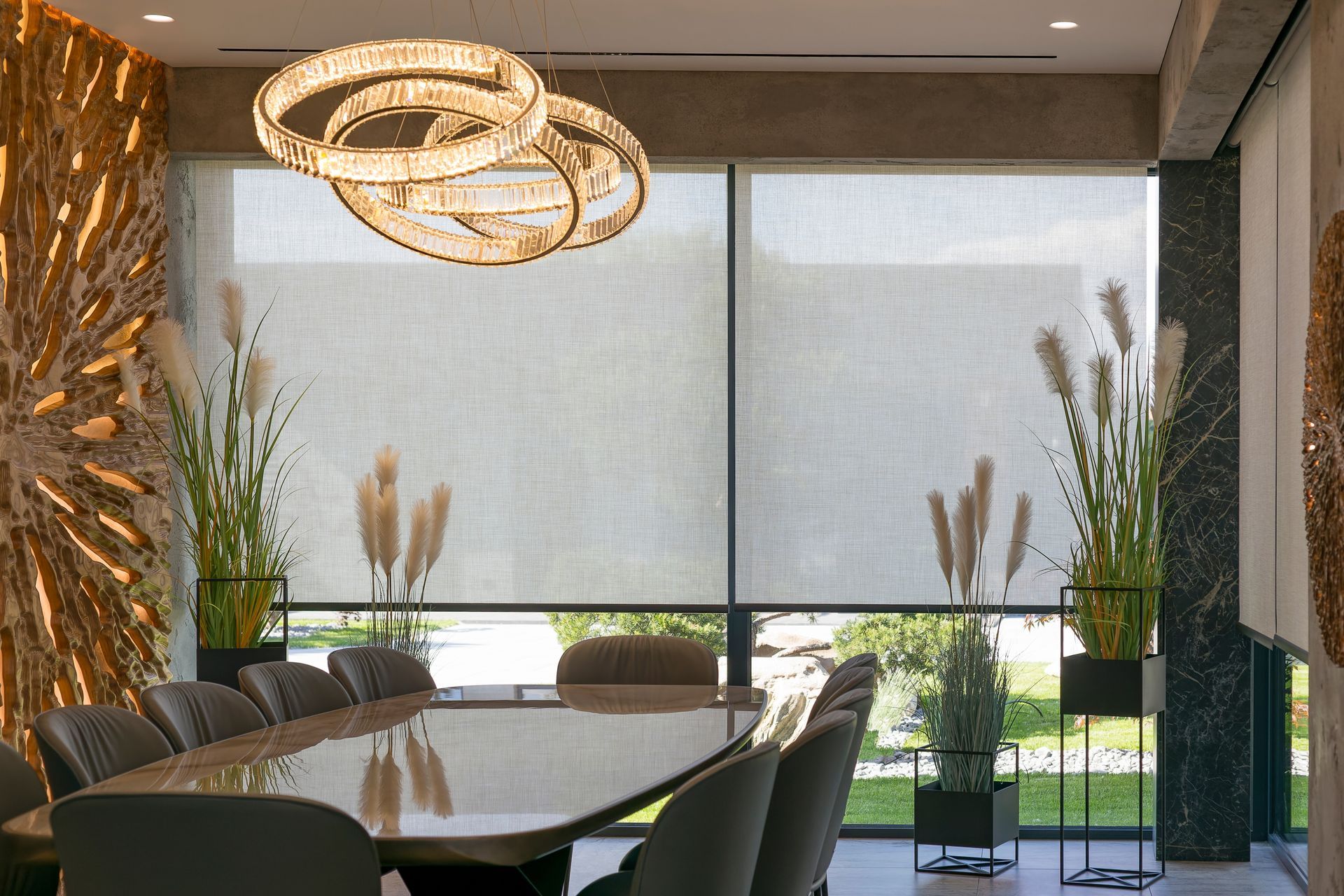 Modern conference room with long table, black chairs, pendant lights, and large windows with shades