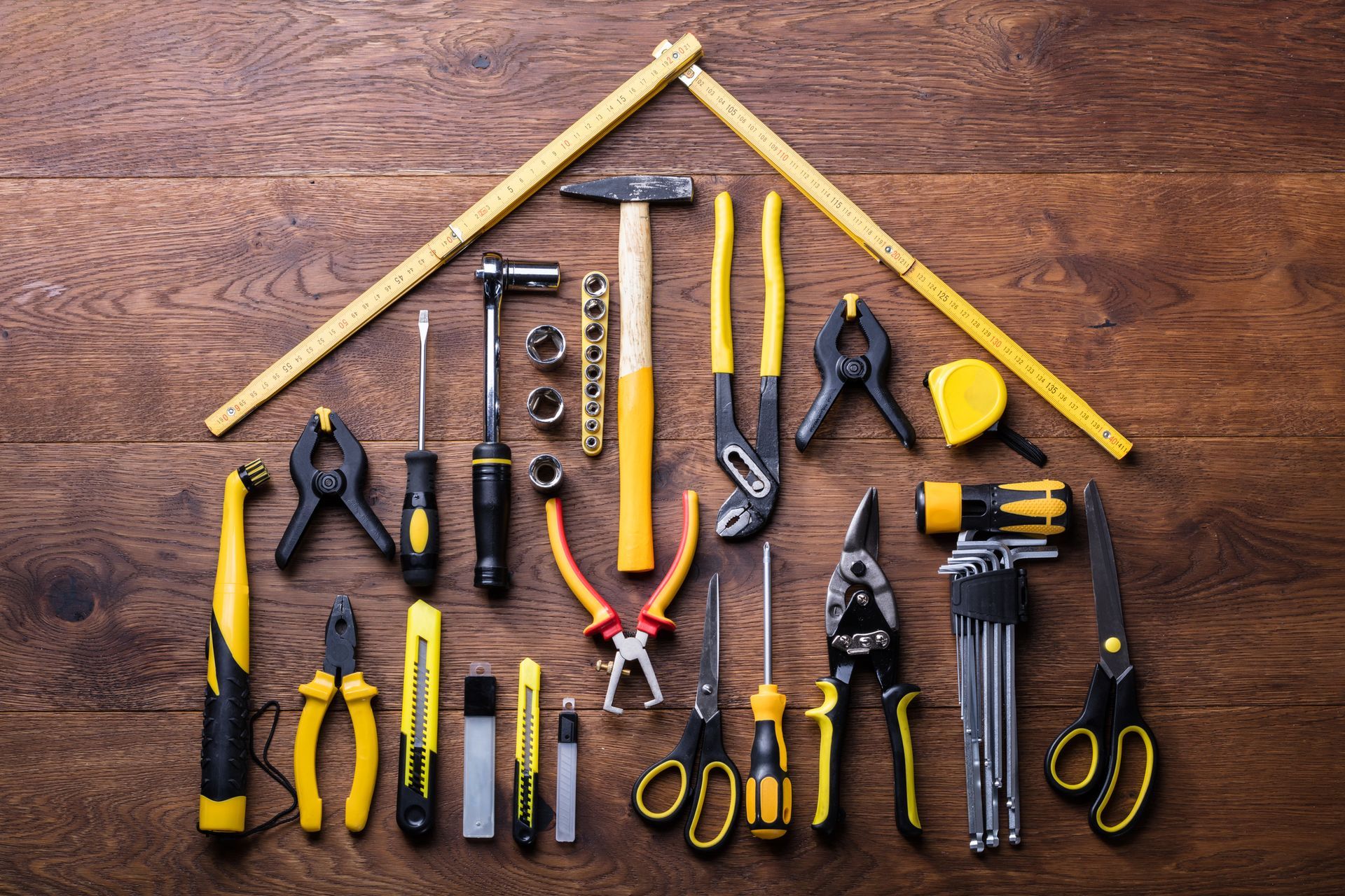 A bunch of tools are arranged in the shape of a house on a wooden table.