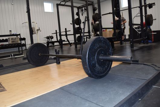 A barbell with black weight plates resting on a lifting platform in a gym.