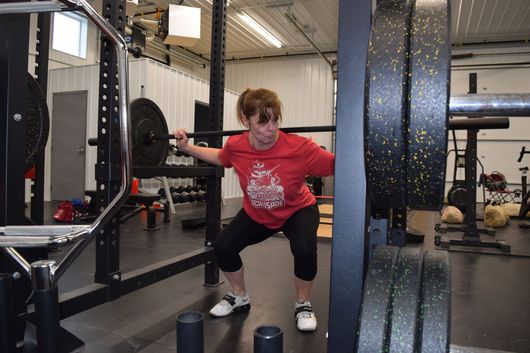 A person in a red t-shirt performing a barbell squat inside a gym squat rack.