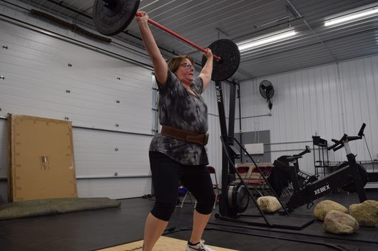 A person lifting a barbell overhead in a gym setting.