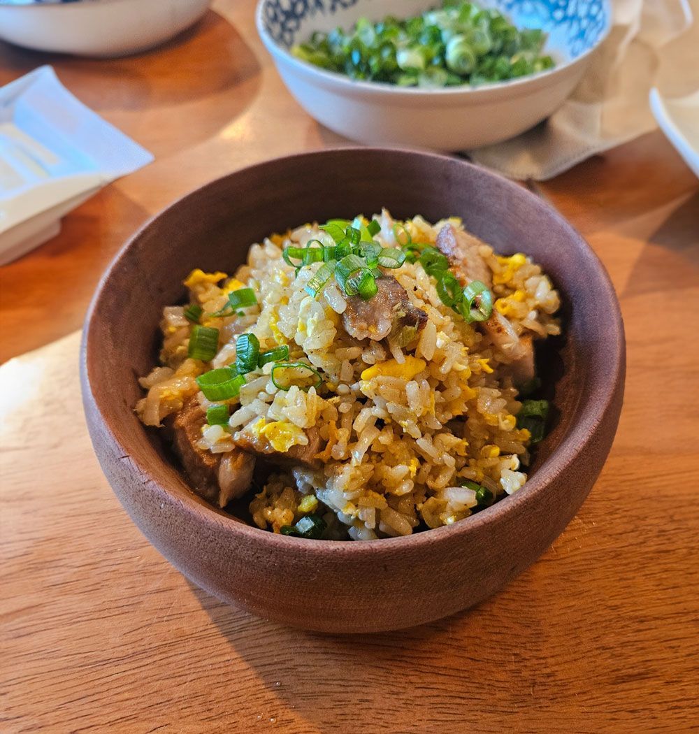A brown bowl of fried rice with egg and scallions, with a small side dish of chopped green onions in the background.