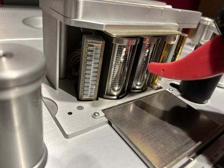 Close-up of a silver machine with open compartments holding cylindrical components; red item points at one.