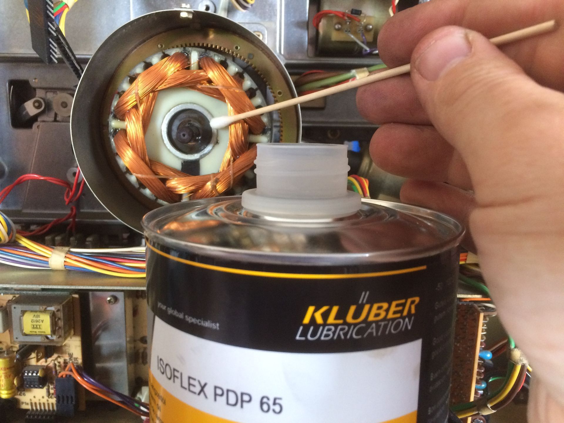 Hand using a cotton swab to apply lubricant from a Klüber Isoflex PDP 65 can onto a motor.