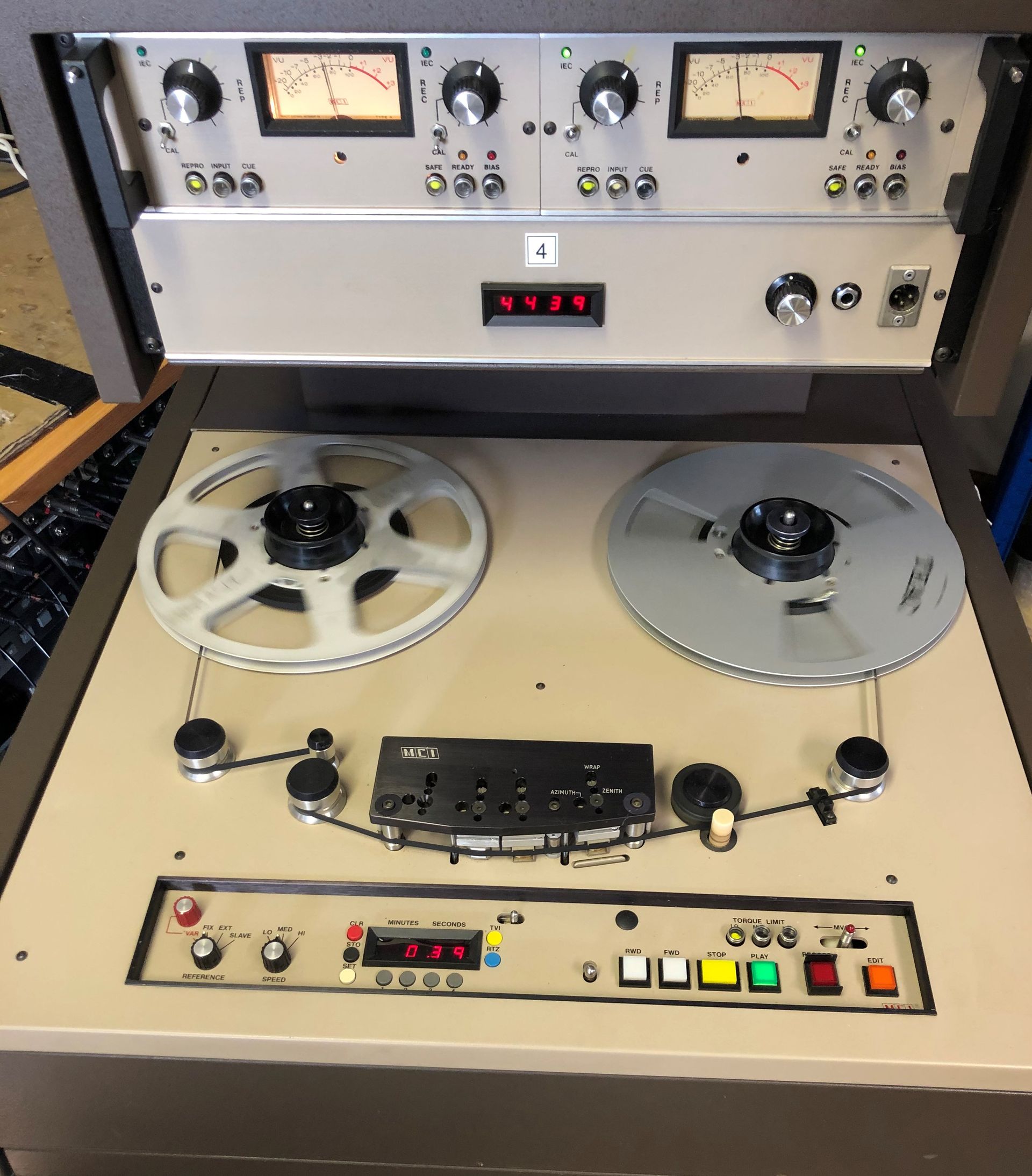 A reel-to-reel tape recorder, beige cabinet, with reels of tape, control panel, and VU meters.