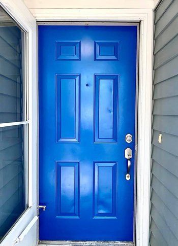 A bright blue door is sitting on a porch next to a window.