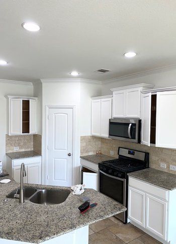 A kitchen with white cabinets , granite counter tops , stainless steel appliances and a sink.