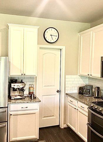 A kitchen with white cabinets , stainless steel appliances and a clock on the wall.