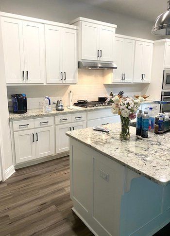 A kitchen with white cabinets , granite counter tops , and a large island.