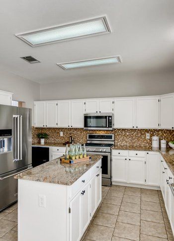 A kitchen with white cabinets , stainless steel appliances , granite counter tops and a large island.