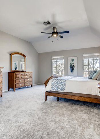 A bedroom with a bed , dresser , mirror and ceiling fan.