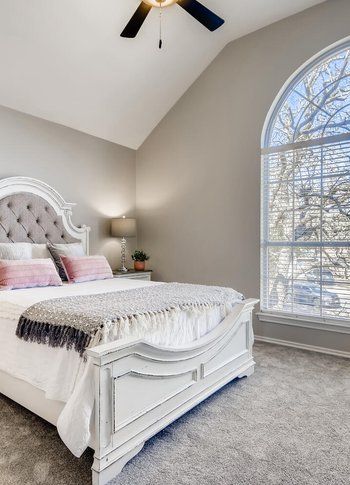 A bedroom with a bed , ceiling fan , and large window.