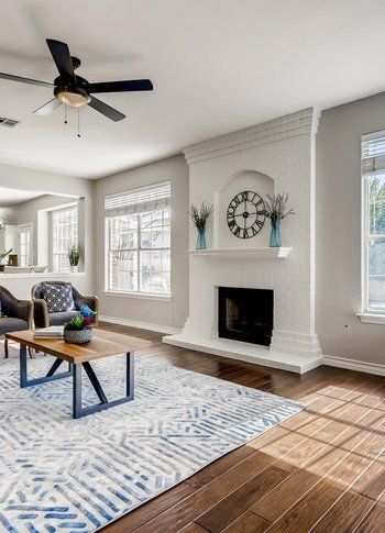A living room with a fireplace , coffee table , chairs and a ceiling fan.