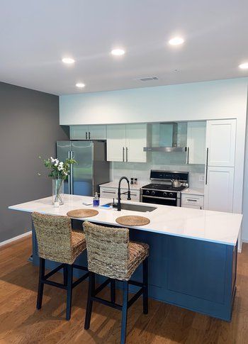 A kitchen with a large island and two wicker chairs.