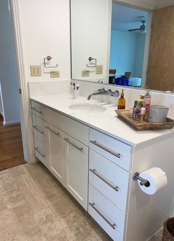 A bathroom with white cabinets , a sink and a mirror.