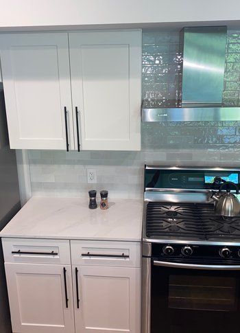 A kitchen with white cabinets , a stove , and a kettle on the counter.
