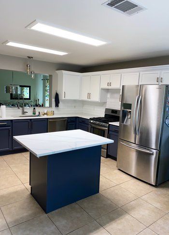 A kitchen with blue cabinets , stainless steel appliances and a large island.