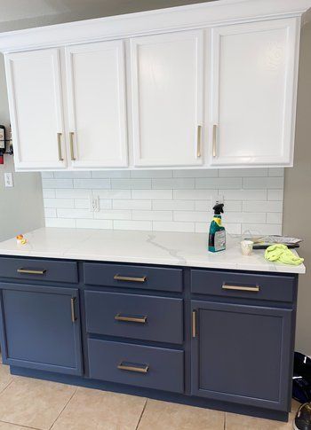A kitchen with white cabinets and blue drawers and a white counter top.