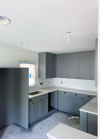 A kitchen with gray cabinets and white counter tops under construction.