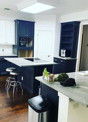 A kitchen with black cabinets and white counter tops and a trash can on the counter.