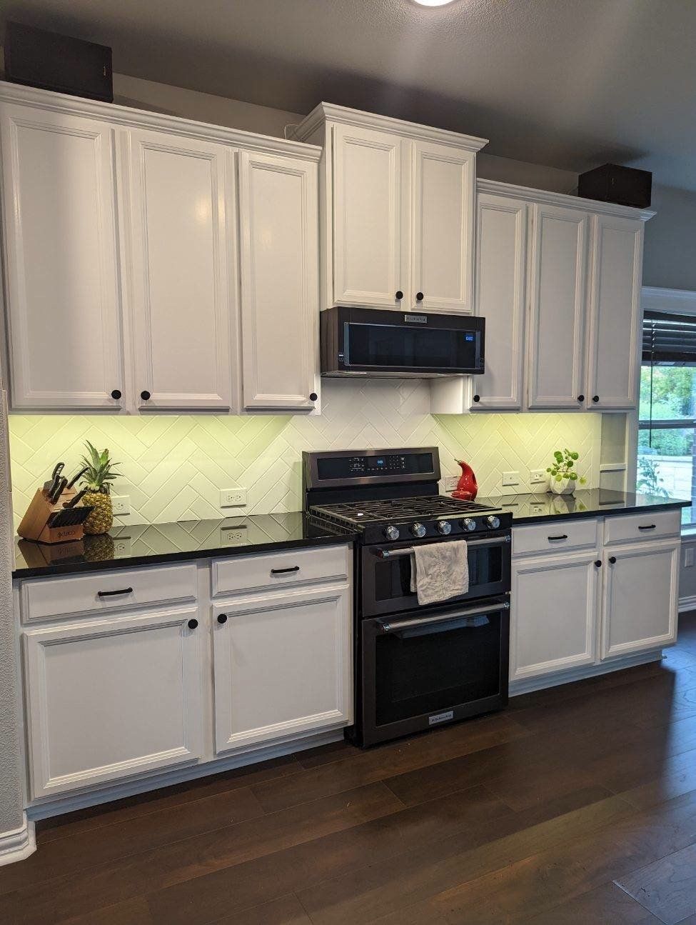 A kitchen with white cabinets , black counter tops , a stove and a microwave.
