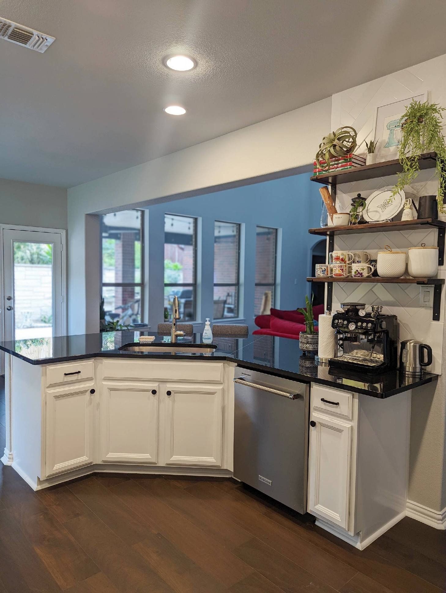 A kitchen with white cabinets , black counter tops , stainless steel appliances and a coffee maker.