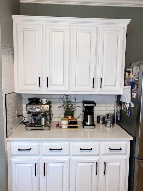 A kitchen with white cabinets , a coffee maker , and a stainless steel refrigerator.