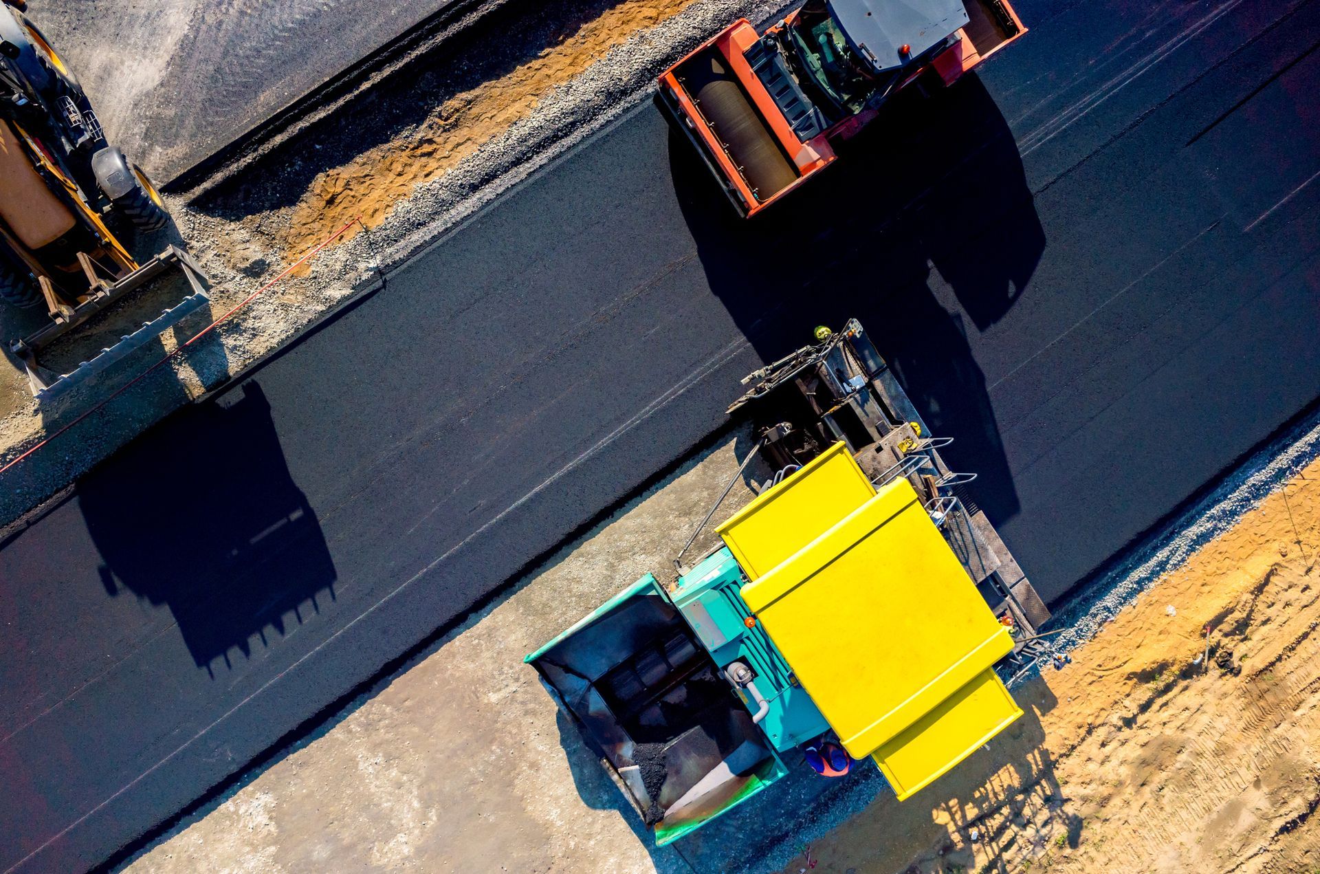 Asphalt paving in progress; machines compacting and laying fresh black asphalt on a road.