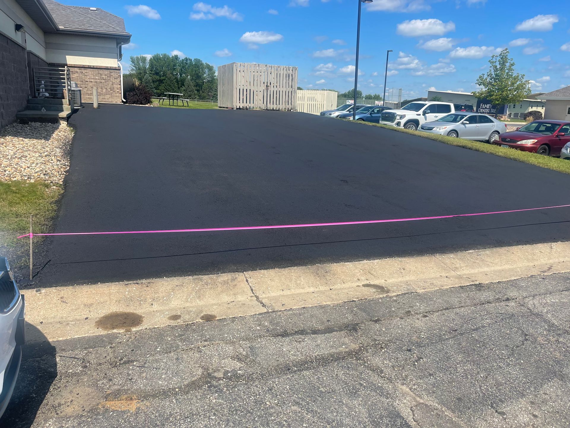 Newly paved black asphalt parking lot with a pink barrier tape line.