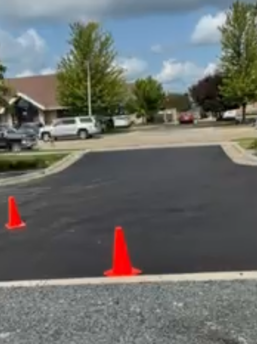 Freshly paved asphalt with orange traffic cones, a car, and a building on a sunny day.