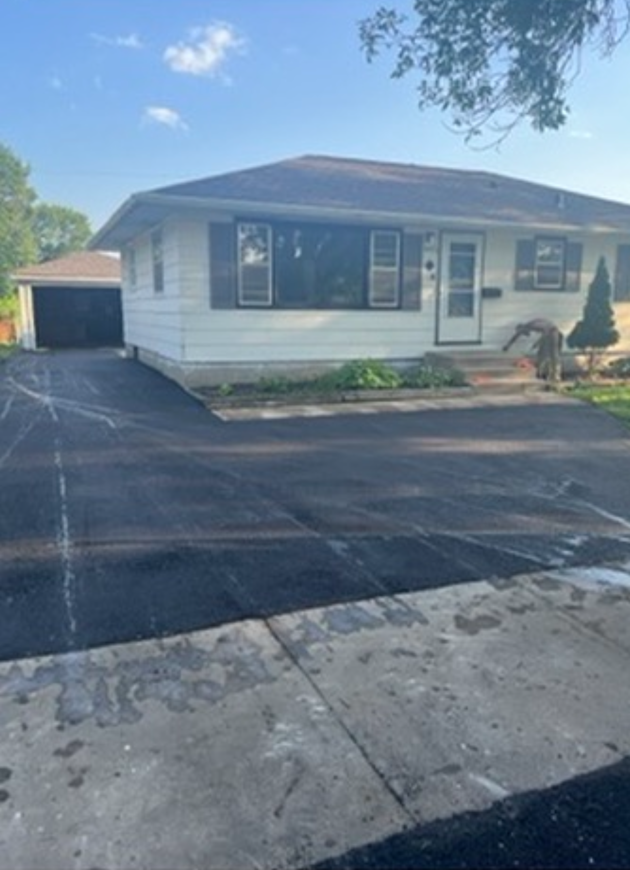 White house with brown roof, black shutters, and newly paved driveway.