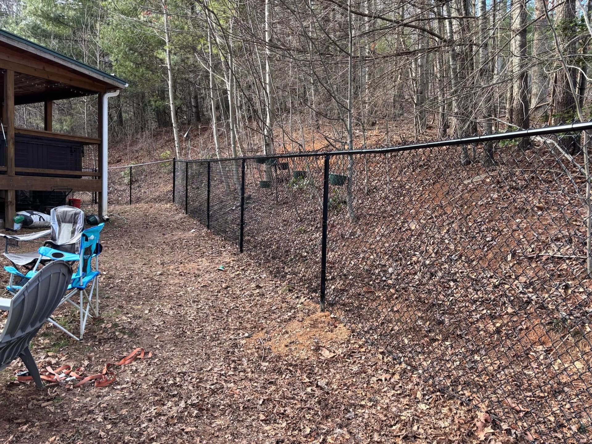 Wooded backyard with a black chain-link fence and patio chairs beside a deck
