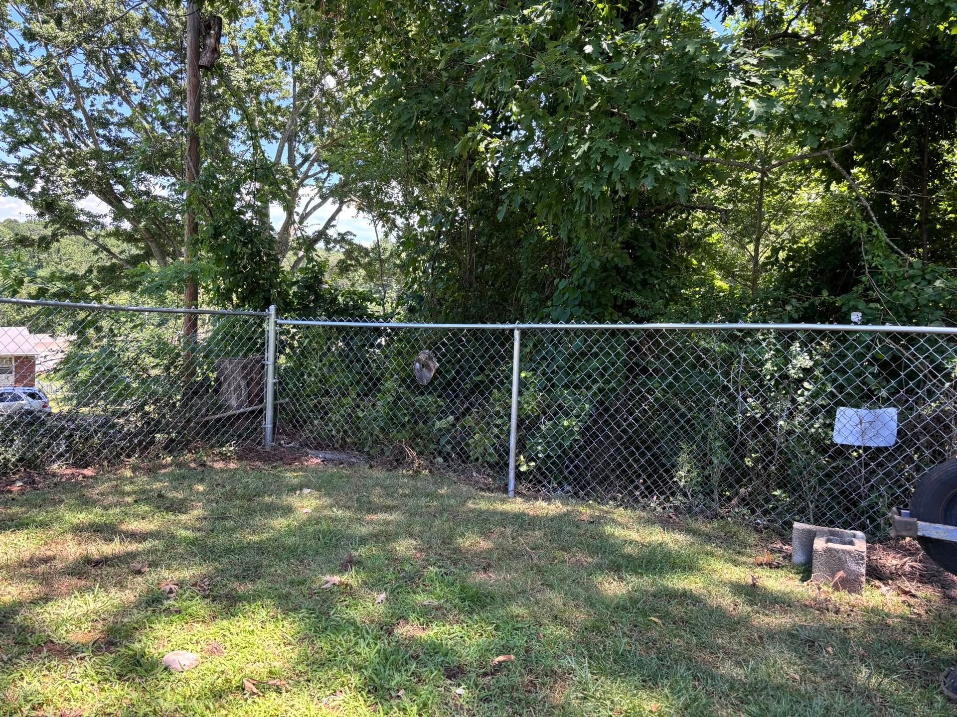 Chain-link fence in a wooded yard with a small sign and cinder blocks on the right.