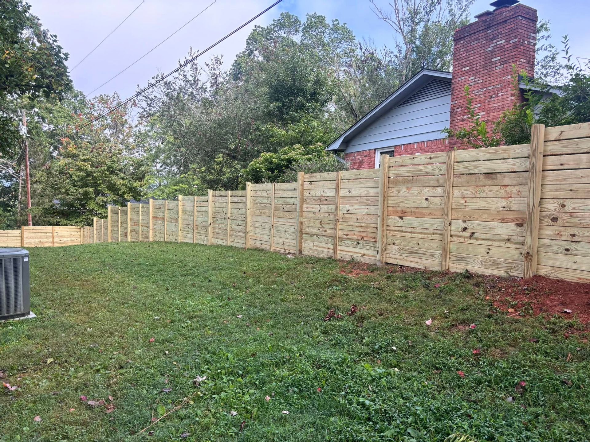 Wooden privacy fence along a grassy yard beside a house with a red brick chimney