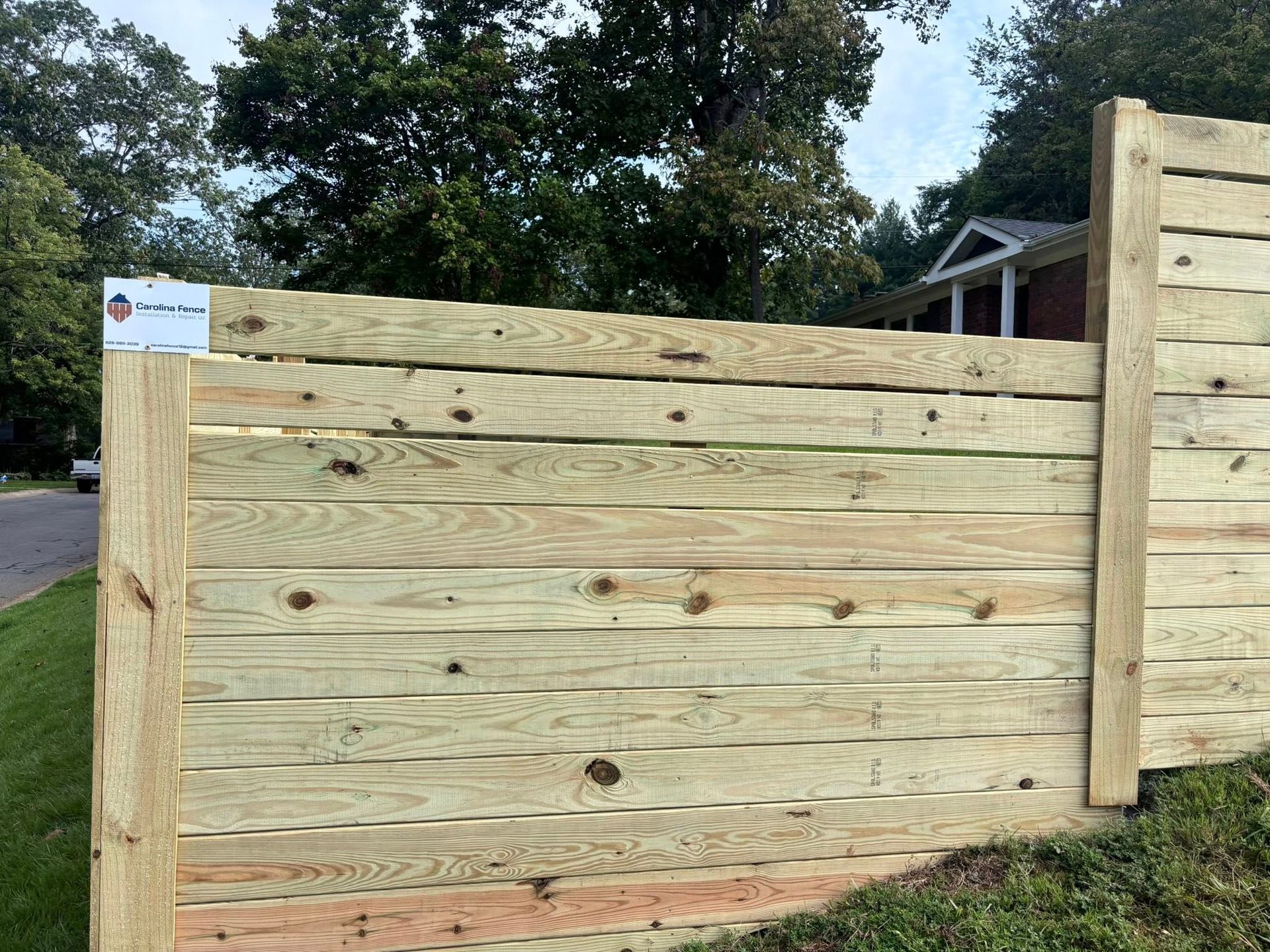 Wooden privacy fence with a gate, set along a roadside under trees