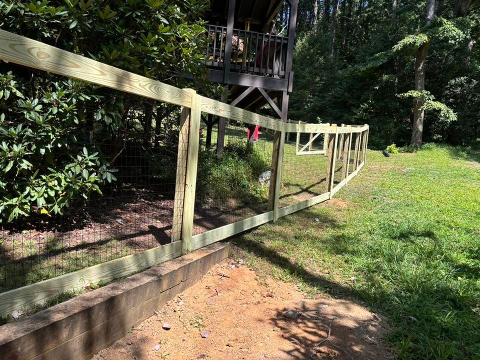 Wooden handrail along a sloped garden walkway beside a grassy yard and dense trees