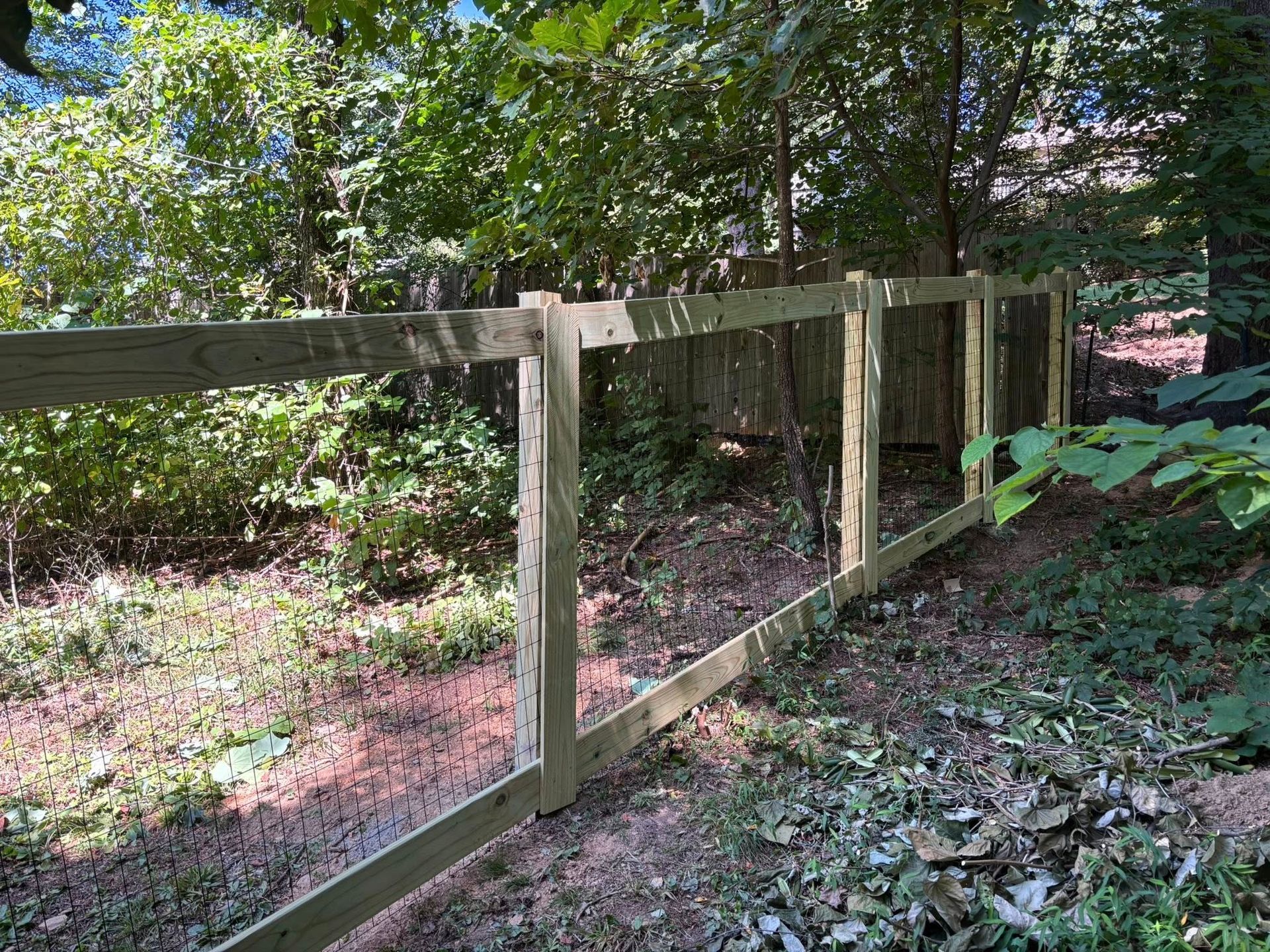 Wooden fence along a shaded wooded path with green foliage