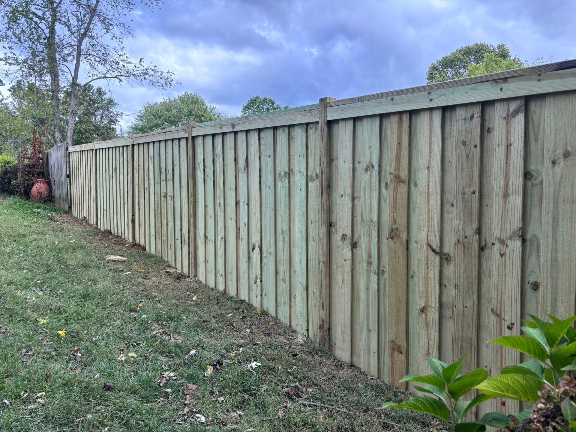 Long wooden fence along a grassy yard under cloudy sky