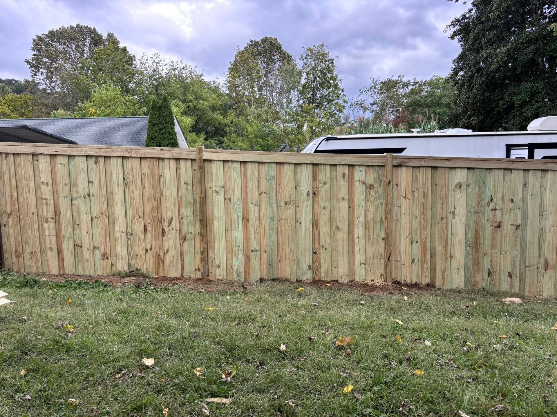 Wooden privacy fence across a grassy yard with trees and a cloudy sky behind it