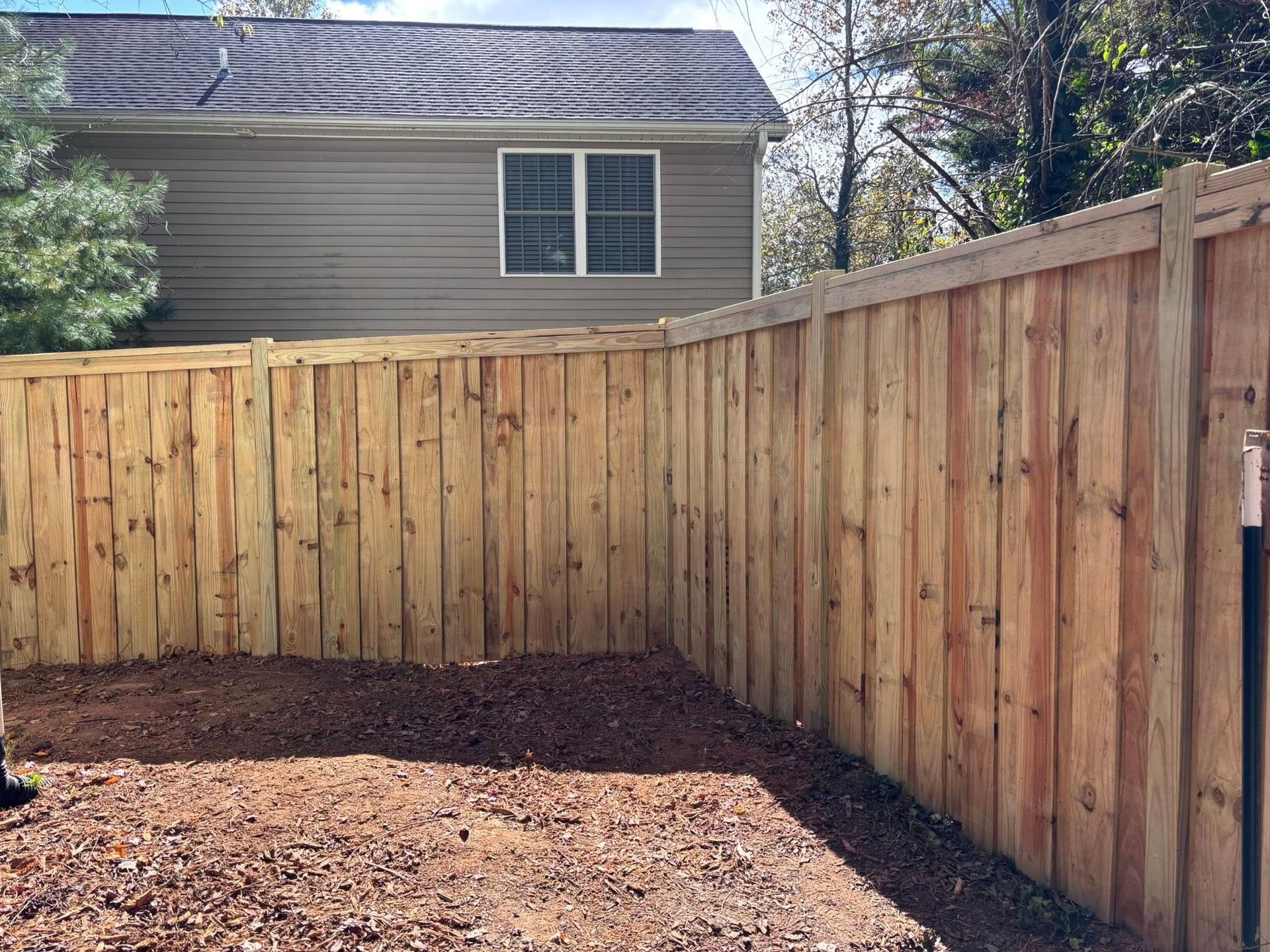 Wooden privacy fence enclosing a small dirt backyard beside a house under cloudy daylight