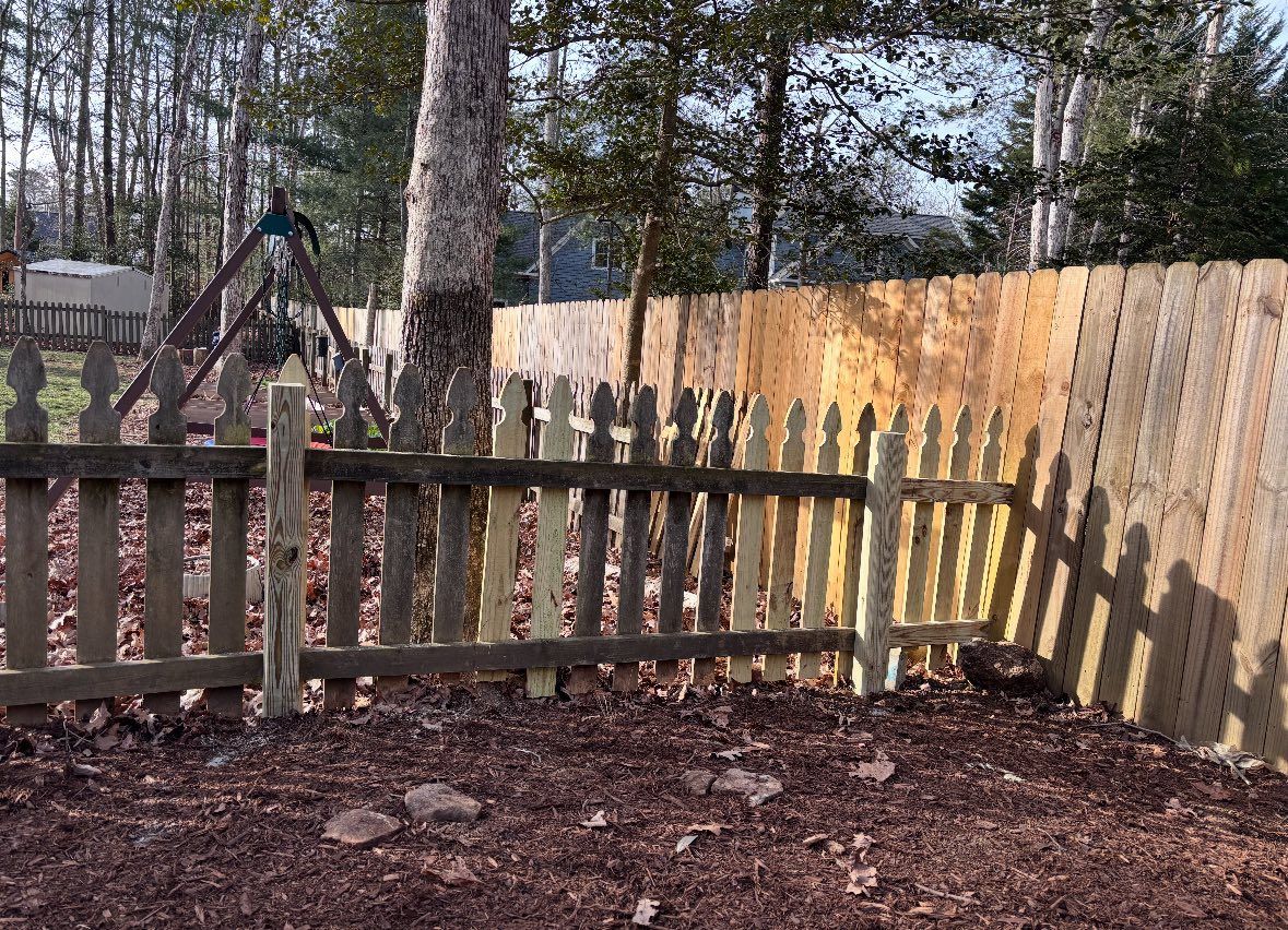 Wooden fence in a wooded backyard with a playground swing set and fallen leaves on the ground