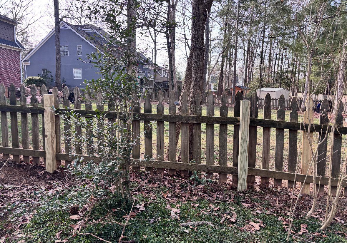 Weathered wooden fence in a wooded backyard with fallen leaves and houses in the background