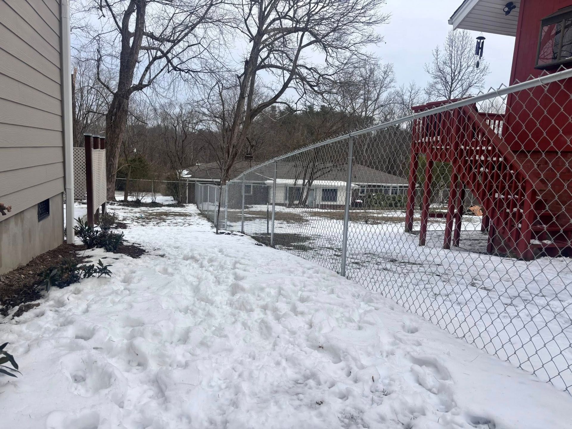 Snowy backyard path beside a house and chain-link fence in winter