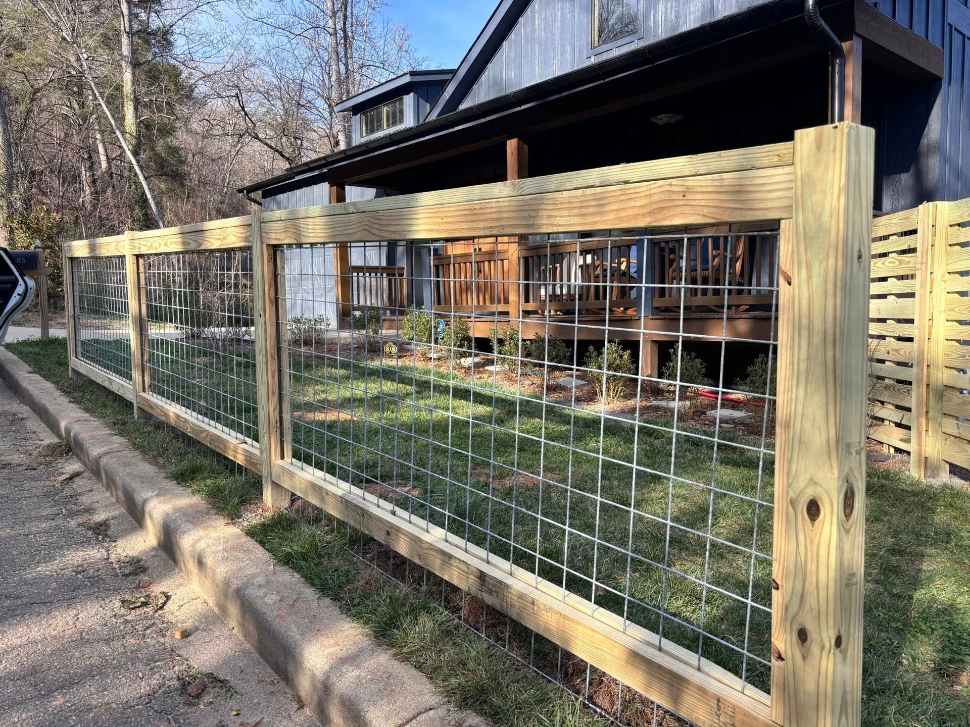 Wooden fence with wire mesh along a yard beside a house, with grass and trees in the background