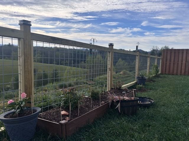 Raised garden beds along a wooden fence overlooking a green valley under a cloudy sky