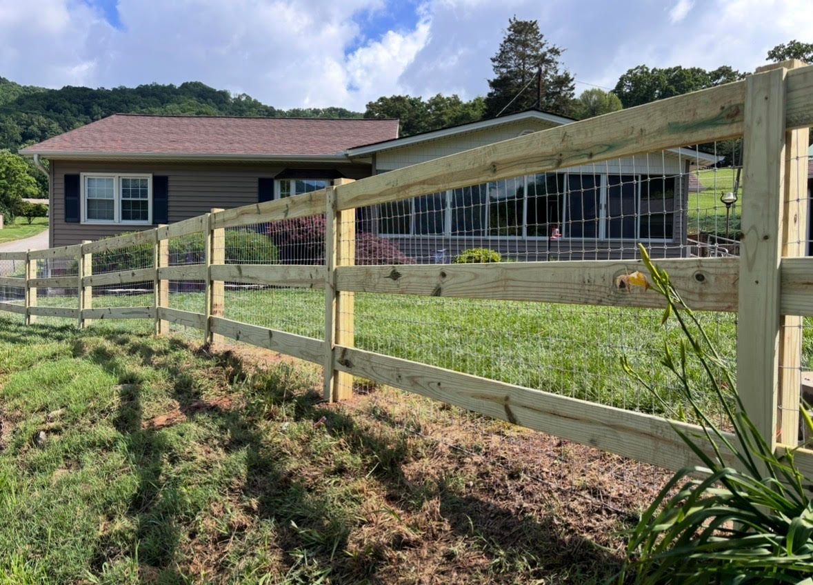 Wooden fence in front of a house with a screened porch and garden under a partly cloudy sky